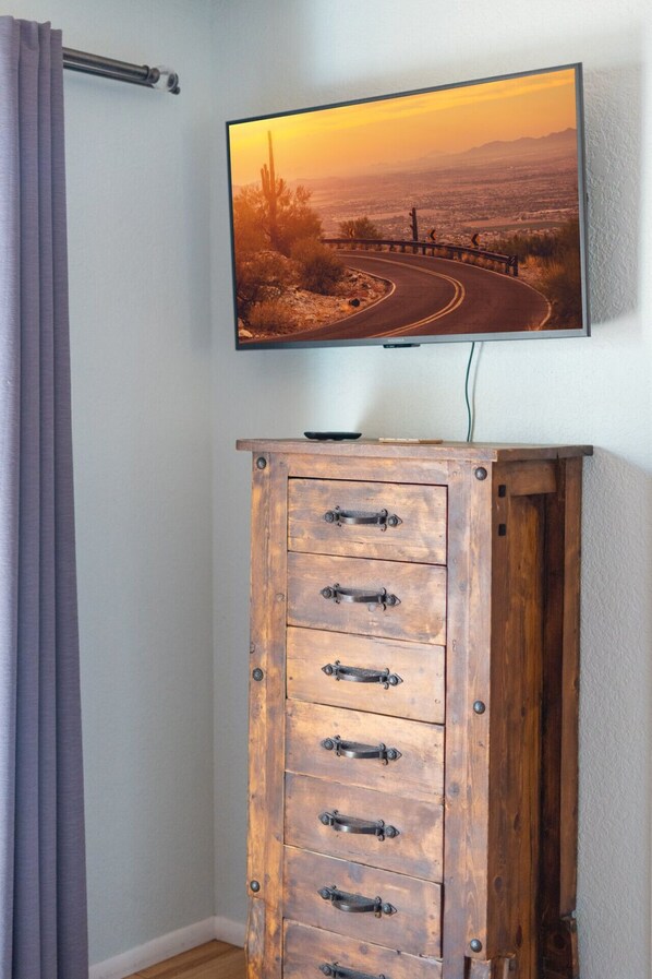 Un téléviseur fixé au mur diffuse une vue panoramique d’un coucher de soleil. En dessous du téléviseur, on trouve un meuble en bois doté de plusieurs tiroirs.
