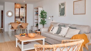Uma sala de estar moderna com um sofá, cadeiras de vime, uma mesa de jantar com frutas e uma estante de livros.
