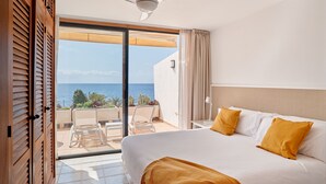 Quarto de hotel com cama grande, ventoinha no teto, vista para o mar e varanda com cadeiras.
