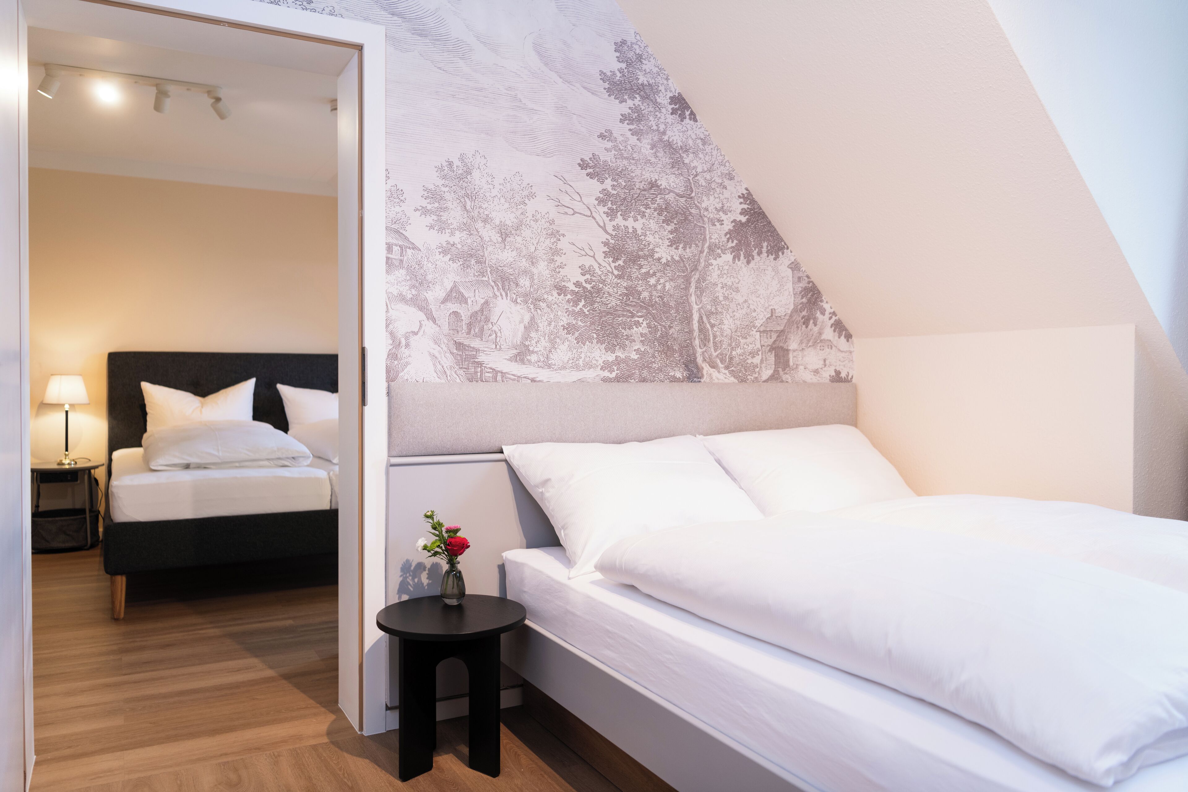 Ein Schlafzimmer mit einem Bett, einem Nachttisch, einem kleinen Tisch mit einer Vase und einer Wand mit einem Wandgemälde zum Thema Natur.