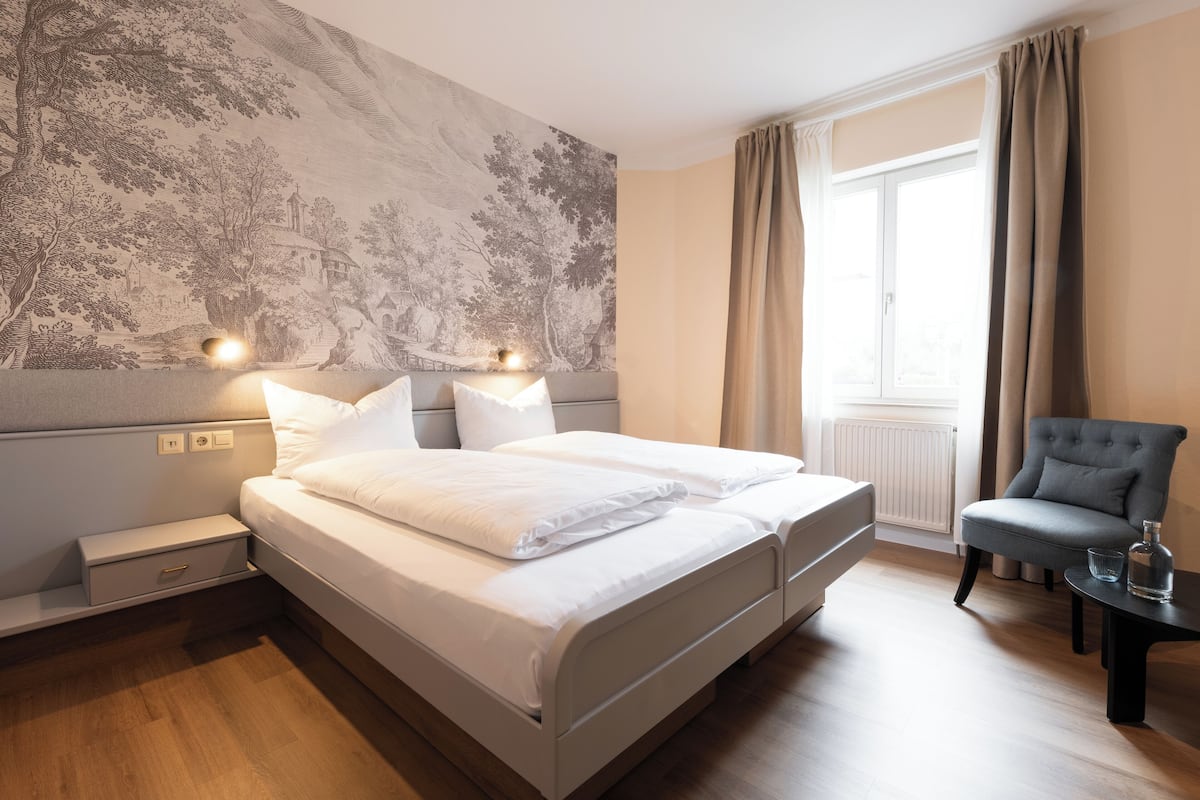 A neatly arranged bedroom with a large bed, bedside tables, a chair, and a window with curtains.