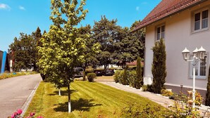 Un barrio residencial con un césped cuidado, un árbol y una casa de techo de tejas.