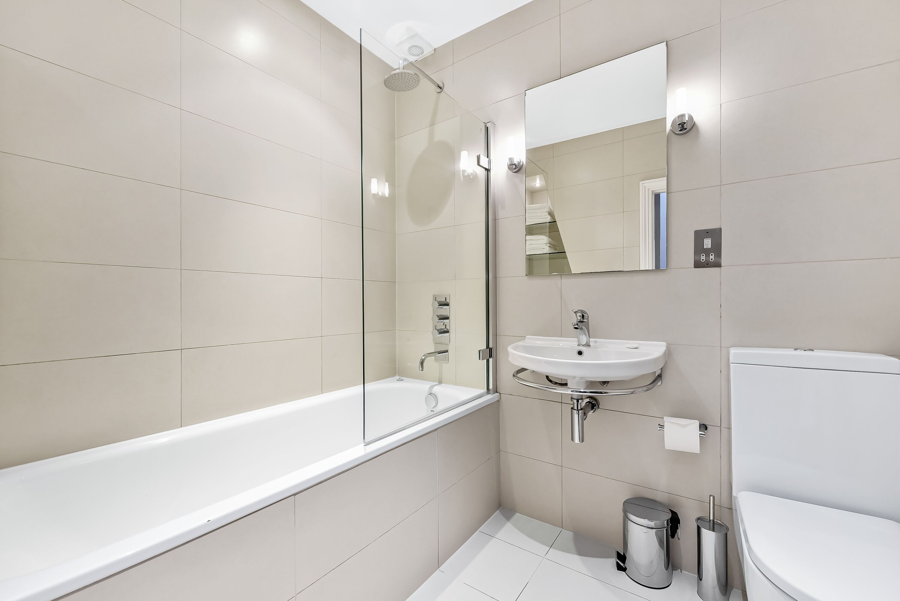 A modern bathroom with a glass-enclosed shower, a white bathtub, a sink, and a toilet.