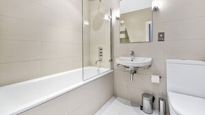 Een moderne badkamer met een douche in een glazen cabine, een witte badkuip, een wastafel en een toilet.