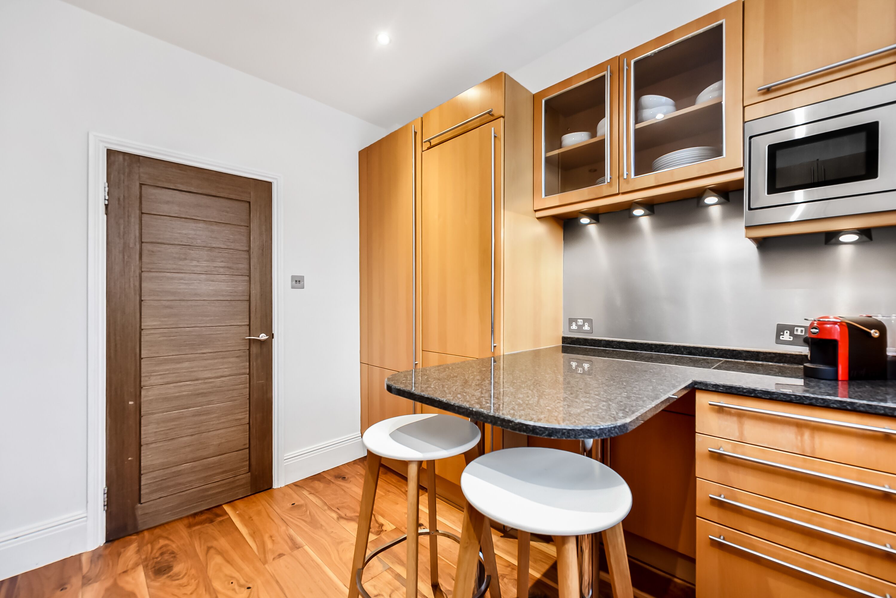 A compact kitchen with wooden cabinets, a built-in microwave, and a granite countertop.