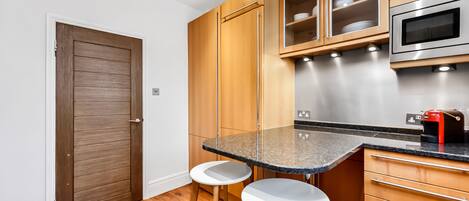 A compact kitchen with wooden cabinets, a built-in microwave, and a granite countertop.