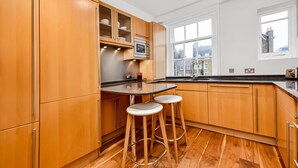 Een moderne keuken met houten kastjes, een magnetron en twee barkrukken.