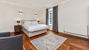 Een moderne slaapkamer met een groot bed, een nachtkastje, een stoel en uitzicht op de stad door een raam.
