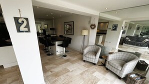 A modern living room with a dining area, featuring a large mirror, a sofa, two armchairs, and a small round table. - North Quay (St Helens)