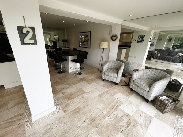A modern living room with a dining area, featuring a large mirror, a sofa, two armchairs, and a small round table.