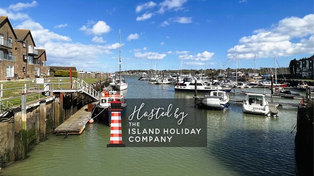 A marina with boats docked, a lighthouse, and residential buildings in the background. - North Quay (St Helens)