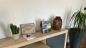A wooden desk with a framed sign, a cactus, a notebook, brochures, and a decorative vase.