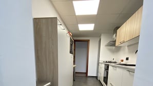 A narrow kitchen with white cabinets, a stainless steel range hood, and a tiled floor.