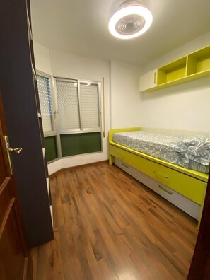 Een slaapkamer met een bed, een raam met zonwering, een plafondlamp en een houten vloer.
