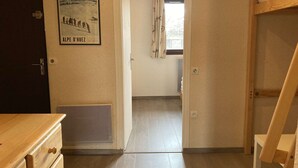 A hallway with a wooden door, a poster on the wall, and a window with curtains.