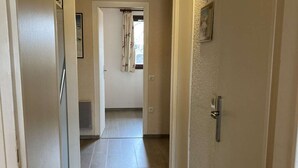 A narrow hallway with a door on the right, a window with a curtain, and a door at the end leading to another room.