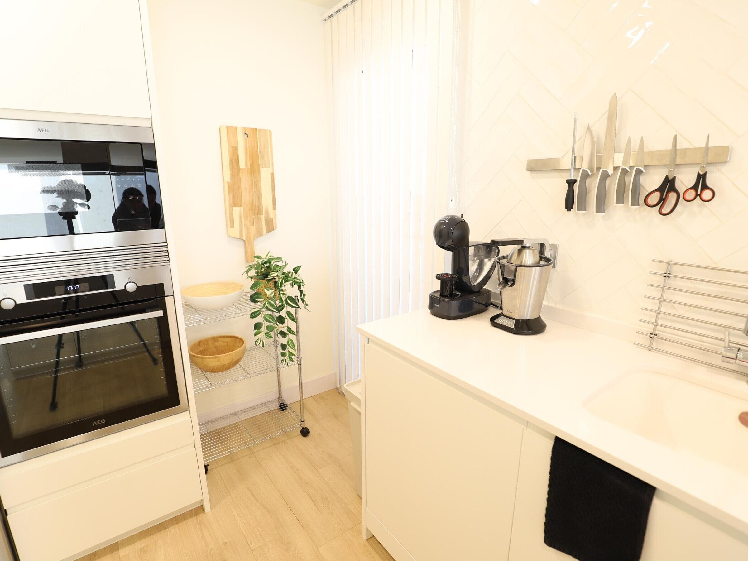 A modern kitchen with an AEG oven, a coffee machine, a hanging knife rack, and a plant.