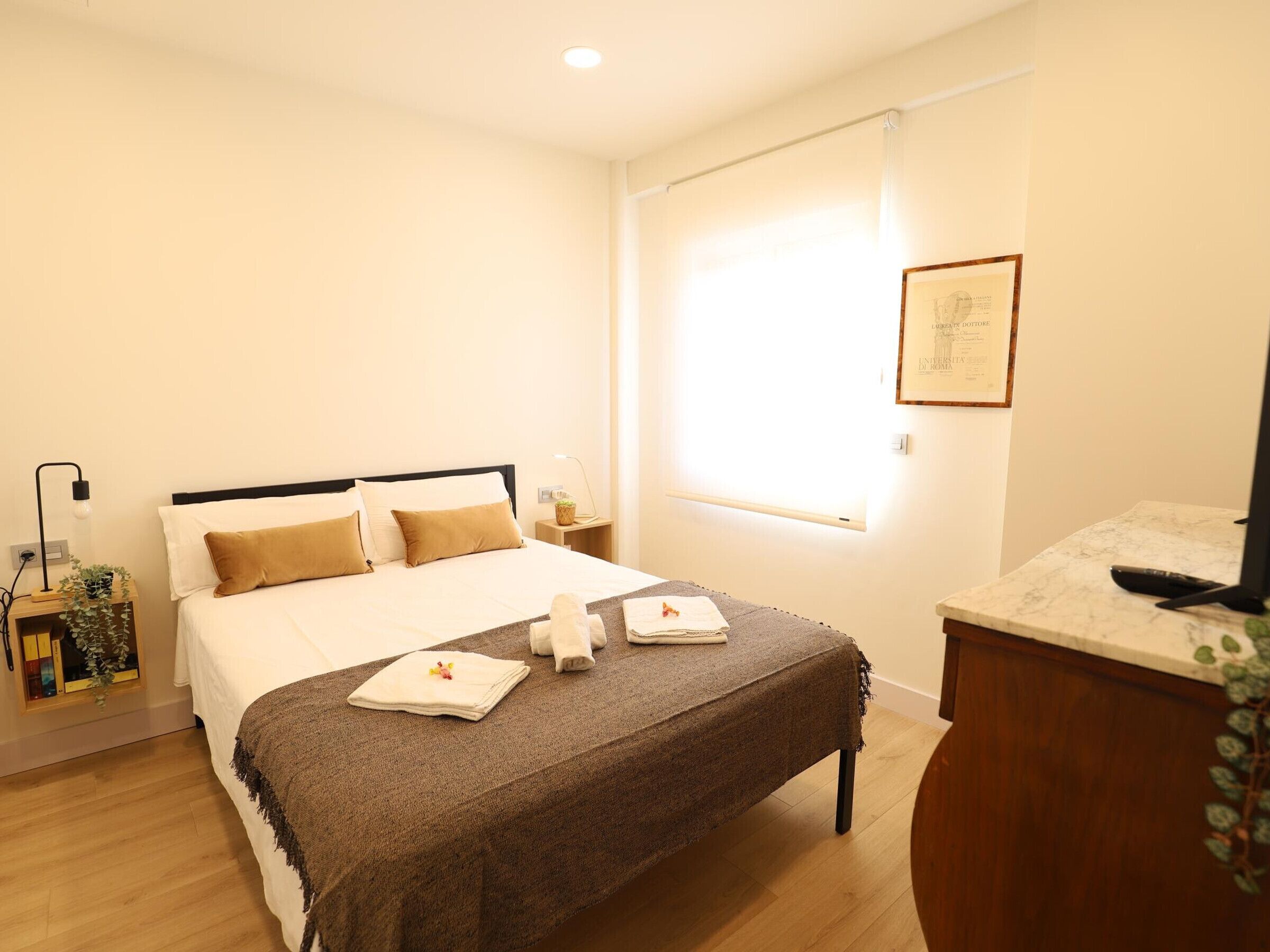 Une chambre d’hôtel avec un lit, des tables de chevet, un bureau et une fenêtre avec des stores.