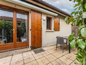 Une maison avec une porte en bois, une fenĂȘtre avec des volets, le numĂ©ro « 92 » sur le mur et une terrasse avec une table et une chaise.