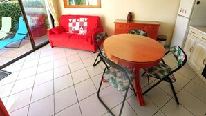 Una habitación con un sofá rojo, una mesa de comedor de madera y sillas con cojines estampados. Hay un mueble pequeño y un microondas sobre una encimera.