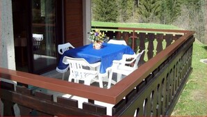 An outdoor patio with a table and chairs, a wooden deck, and a view of a forested area.