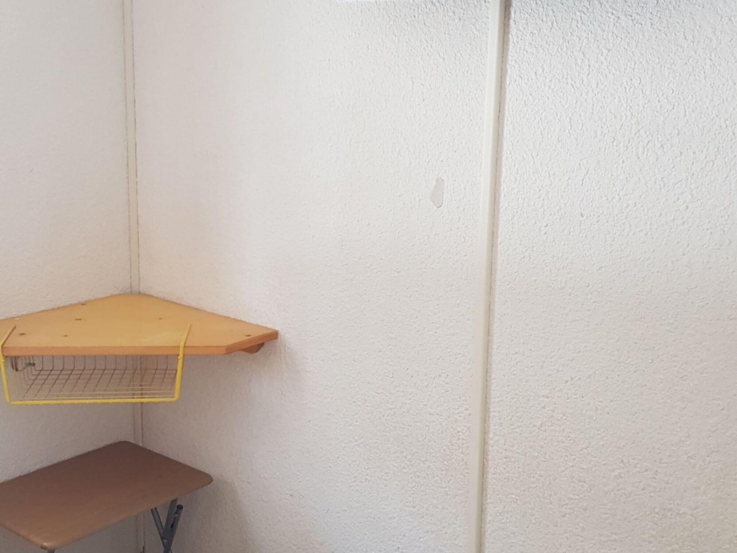 Huoneen nurkka, jossa on valkoinen, kuvioitu seinä, puinen hylly ja ruskea penkki.