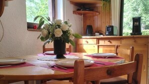 A wooden dining table with plates, a vase of white flowers, and a coffee maker in the background.