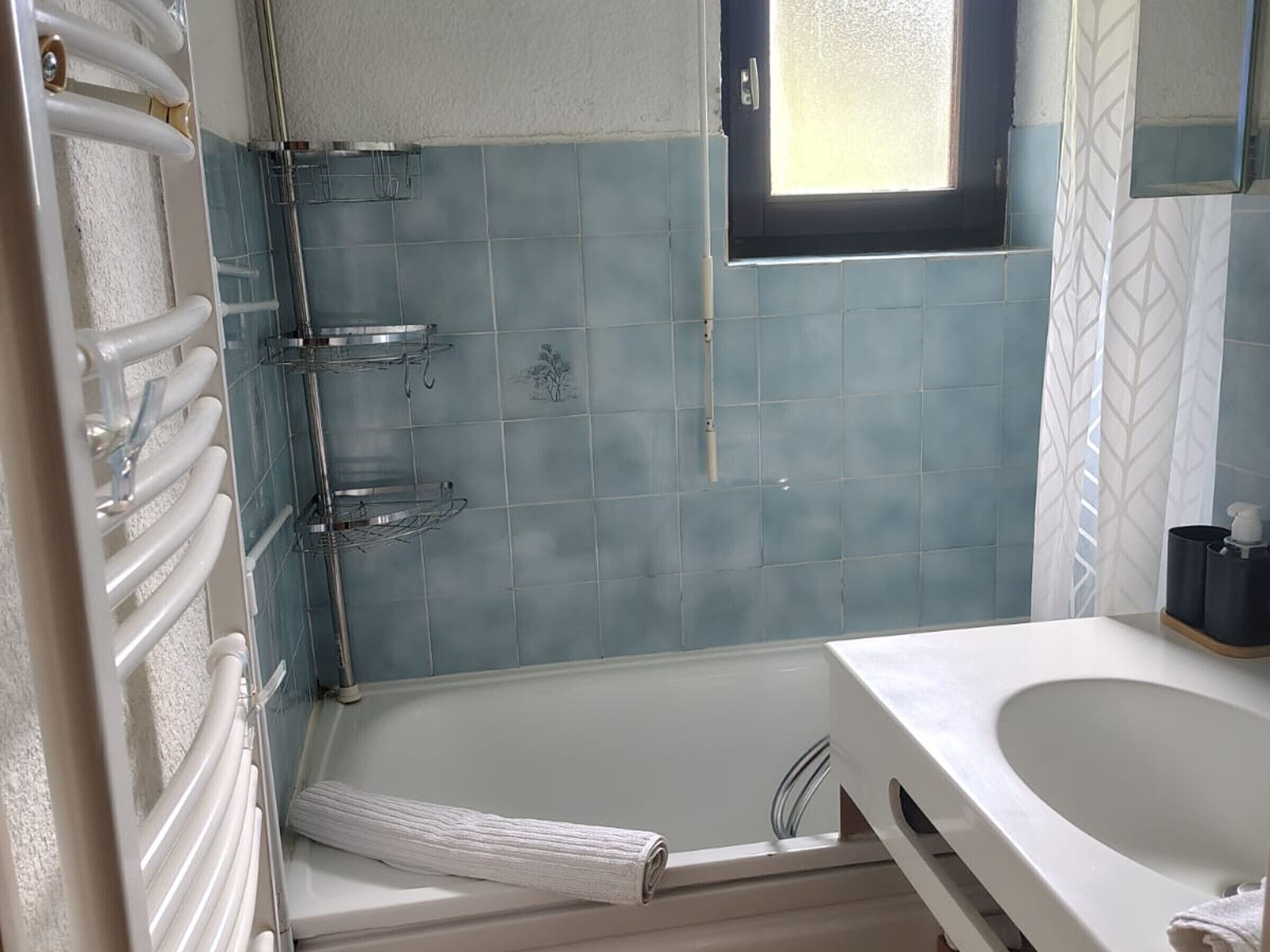 Un baño con bañera, ducha, ventana y un perchero para toallas.