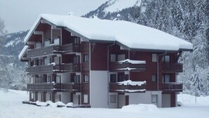 A multi-story hotel with balconies, surrounded by snow-covered trees and mountains.