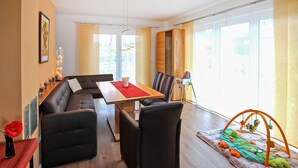 Ein modernes Wohnzimmer mit Sofa, Esstisch, Stühlen und einer Spielecke für Kleinkinder.