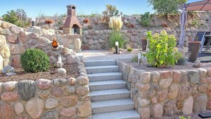 Eine Steintreppe führt zu einem rustikalen Außenbereich mit Schornstein, Blumentöpfen und einer Pergola.