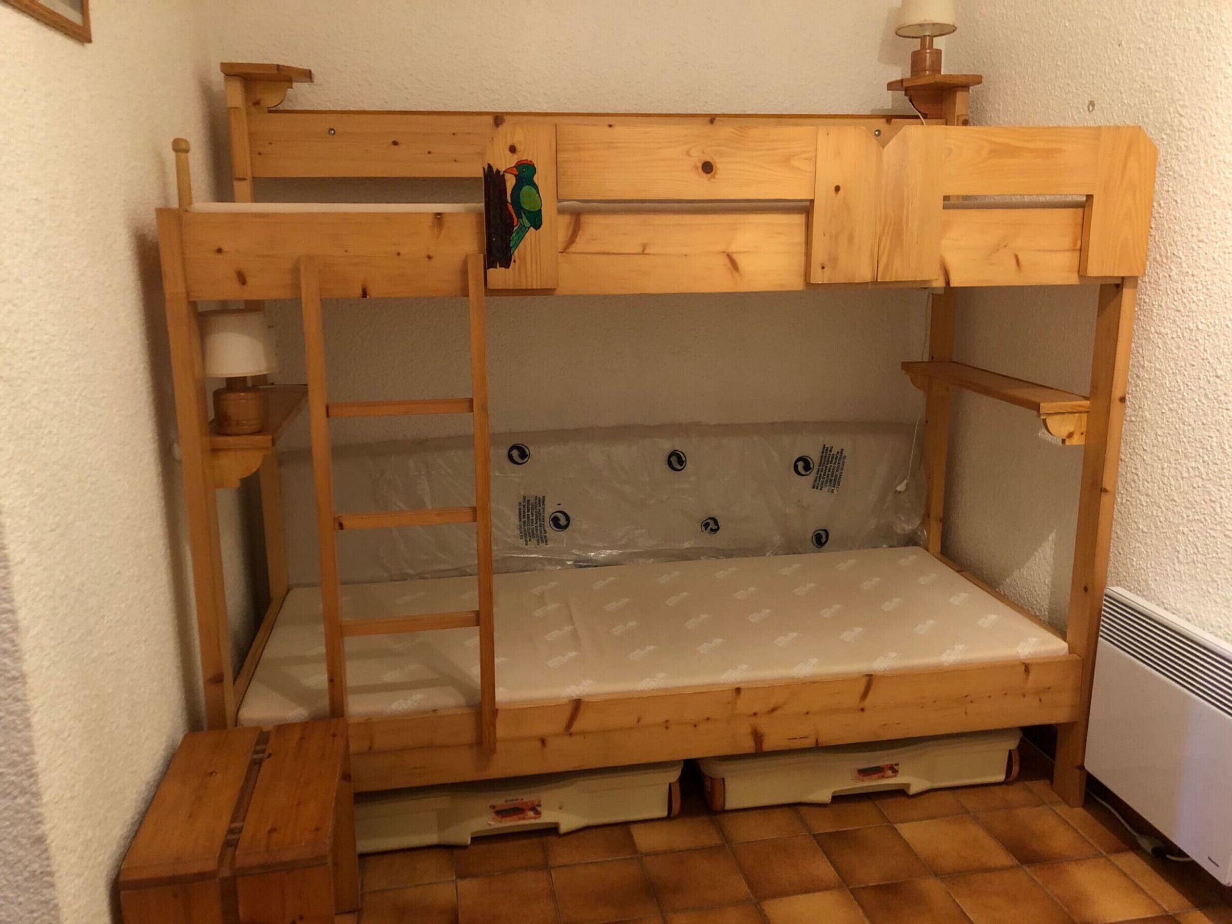 Cama litera de madera con escalera y una pequeña repisa con lámpara.