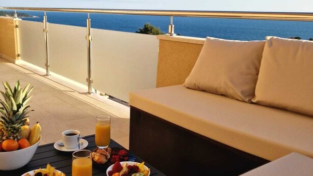 Ein Balkon mit Meerblick, einer Couch und Frühstücksangeboten, darunter Obst, Gebäck und Getränke.