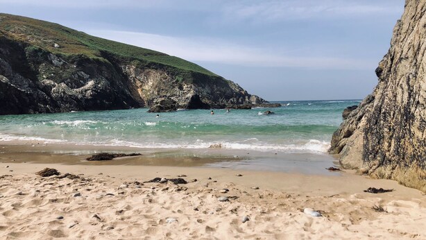 Uma praia de areia com falésias rochosas e mar calmo.