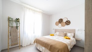 A bedroom with a bed, a bedside table, a lamp, a window with curtains, and a wall-mounted decoration.