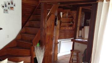 Un'accogliente zona giorno con una scala in legno, un tavolino in vetro con un telecomando e, sullo sfondo, un angolo cottura.