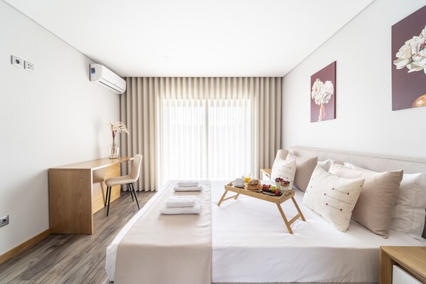 A modern hotel room with a wooden desk, a sofa, a dining table with breakfast, and a large window with curtains. - Casa Eido Doce by House and People (Barcelos)