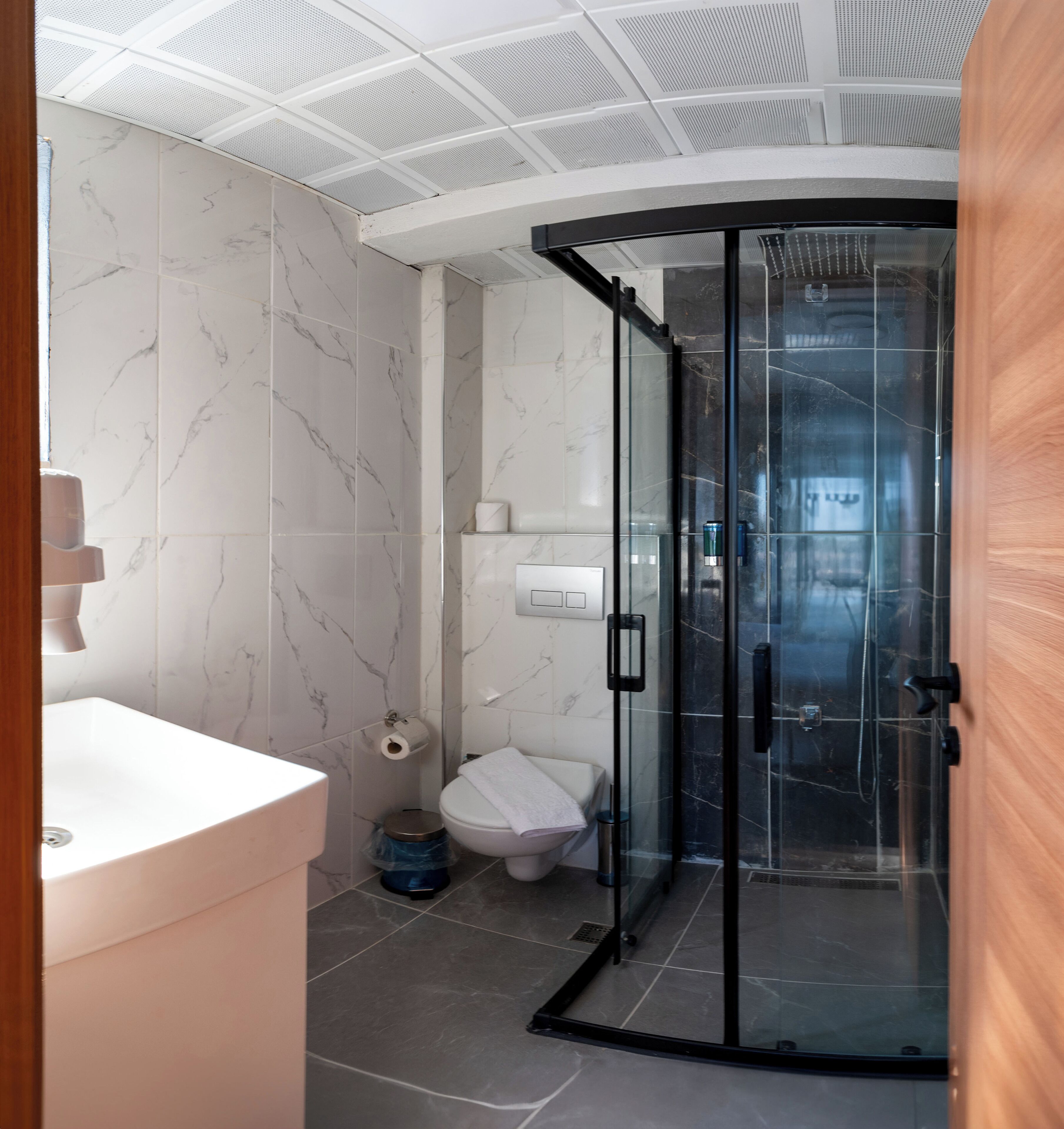 A modern bathroom with a glass shower enclosure, a white toilet, and a marble-tiled wall.
