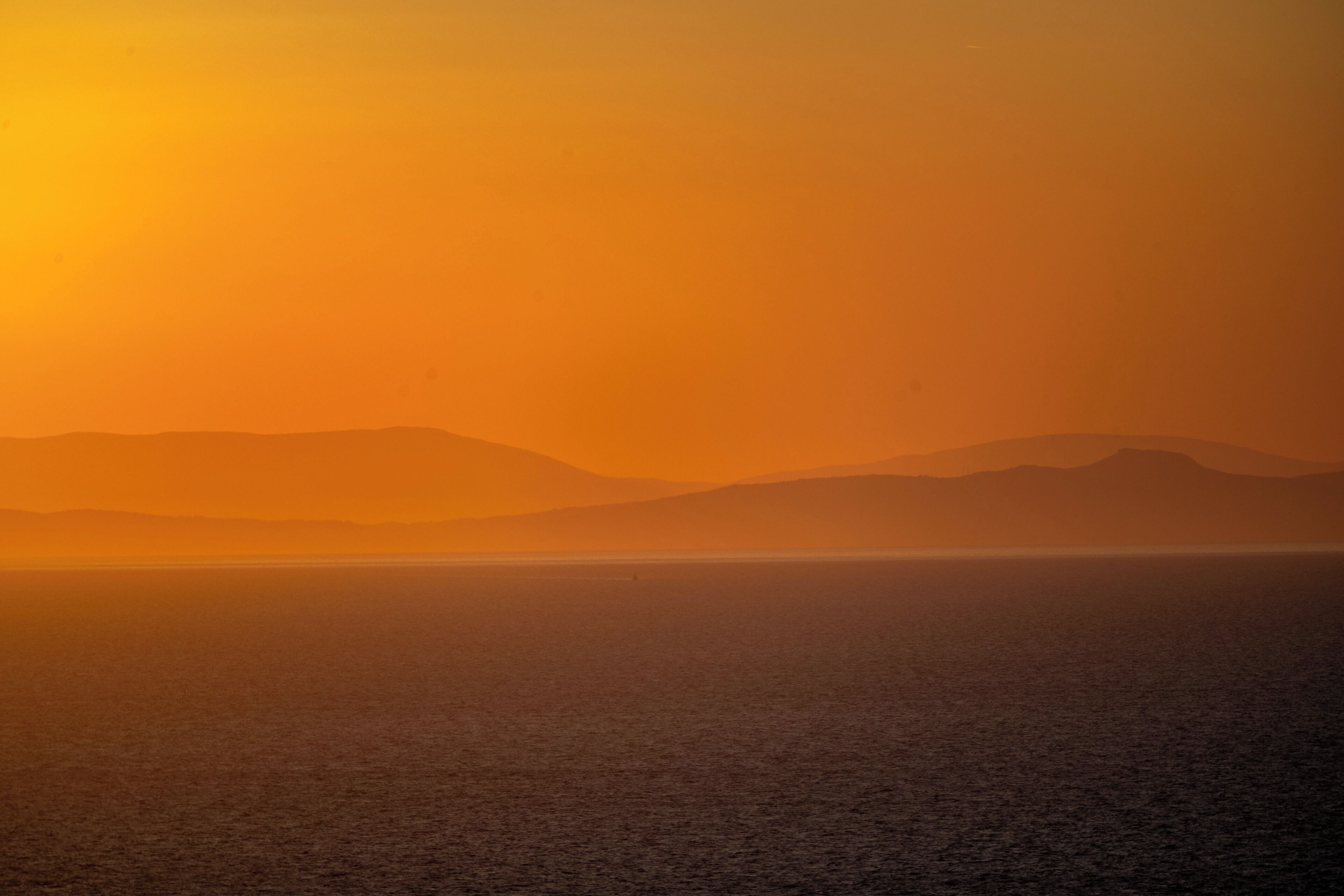 A coastal landscape with a sunset over the sea and distant mountains.