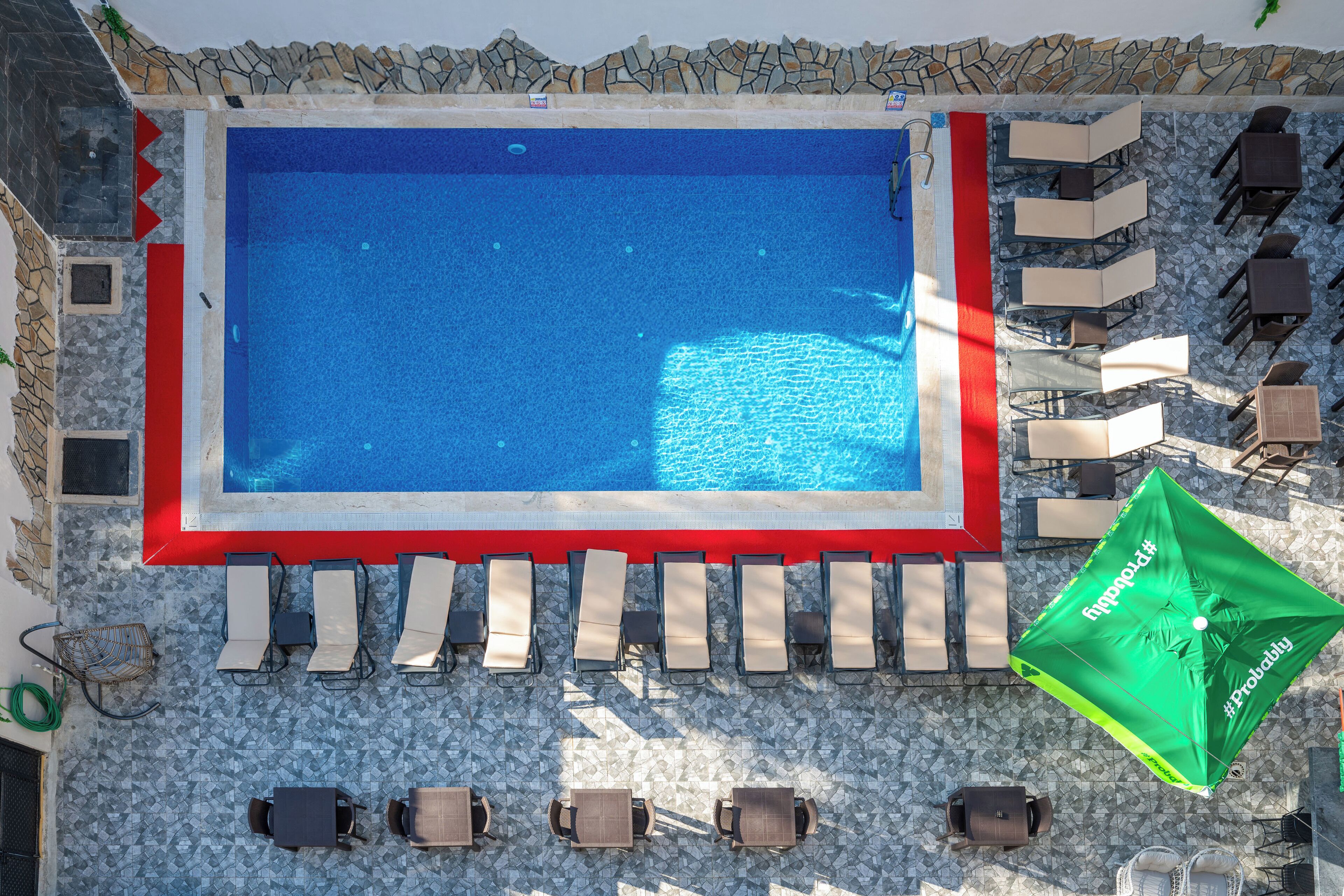Piscina en la azotea con pared de piedra, sillas de descanso y sombrillas.