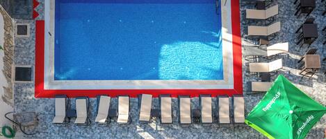 Piscina en la azotea con pared de piedra, sillas de descanso y sombrillas.