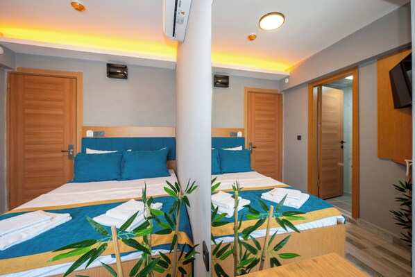 A hotel room with two beds, wooden doors, a flat-screen TV, and a plant.