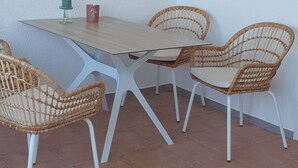 A dining area with a wooden table, four wicker chairs, a wall clock, and two framed artworks.