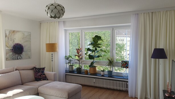 A modern living room with a beige sofa, a floor lamp, and a large window with curtains.