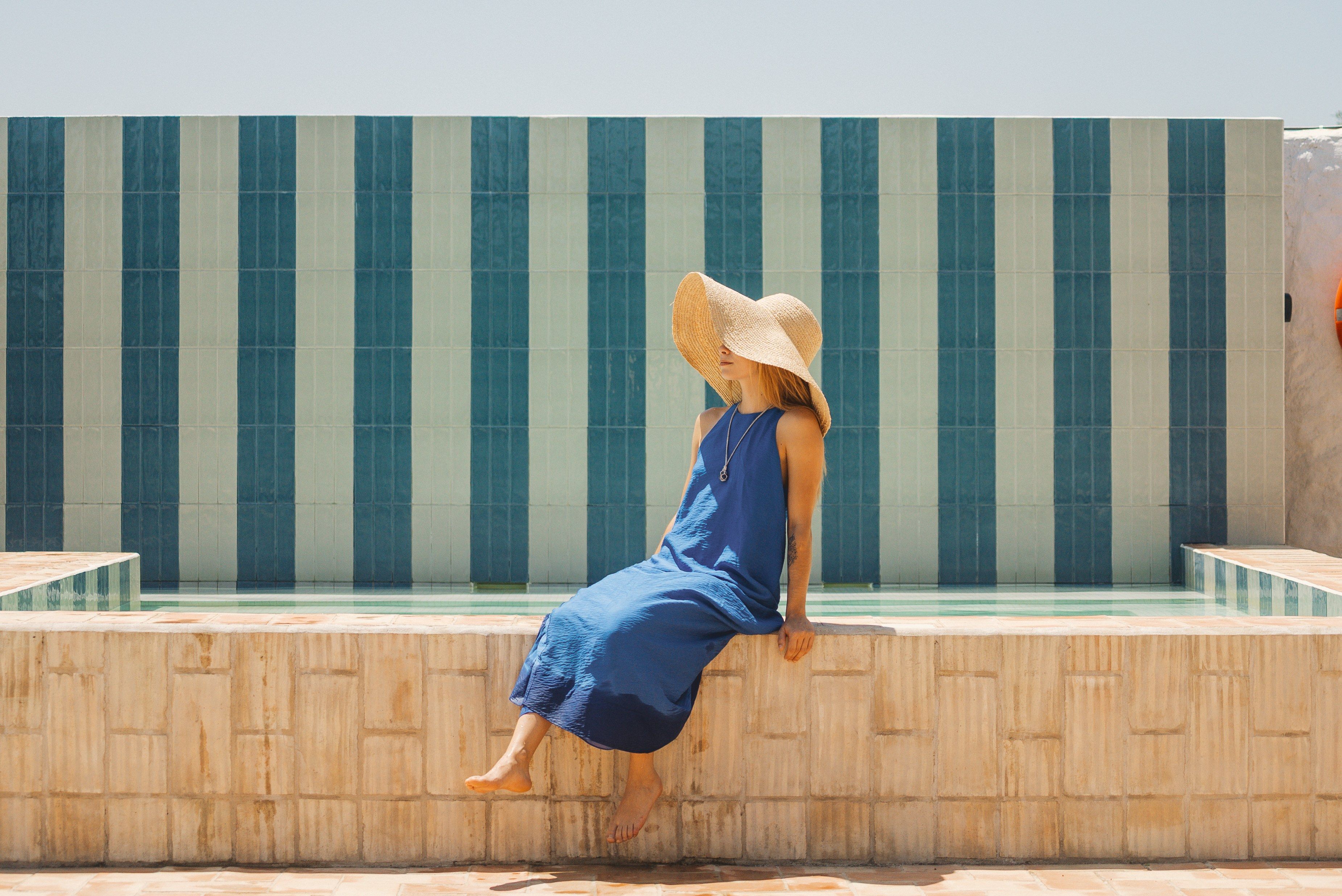 A person sitting on a poolside ledge with a tiled wall in the background.