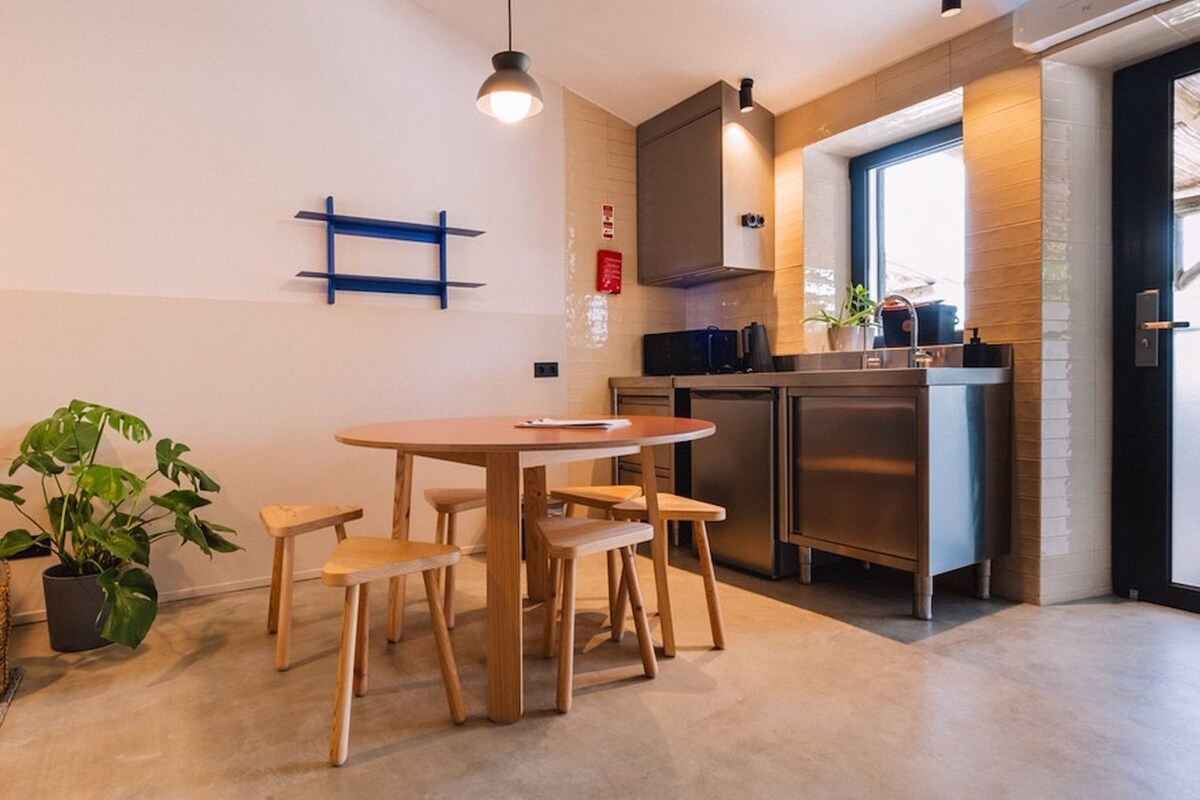 A compact kitchen with a round wooden table and chairs, a hanging light fixture, and a potted plant.
