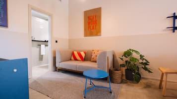 Una sala moderna con un sofá, una mesa de centro azul, una planta en maceta y un banco de madera.