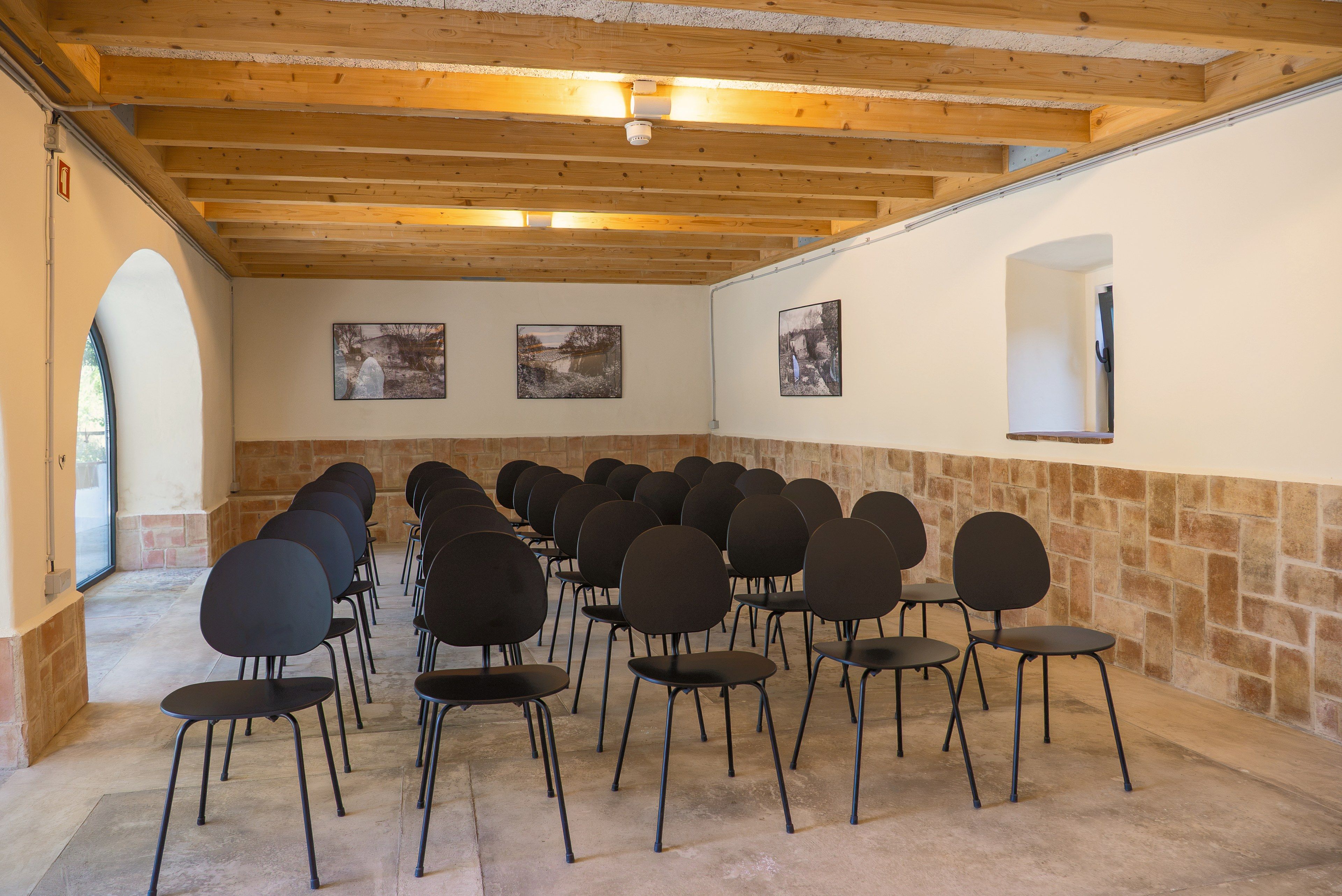 A conference room with rows of chairs, wooden beams on the ceiling, stone walls, and framed pictures on the walls.