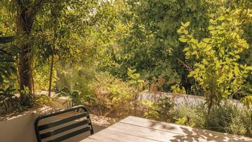 A wooden table with a metal chair in a garden area with dense foliage and a stone wall in the background.
