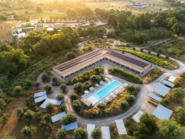 An aerial view of a resort with a swimming pool, covered outdoor seating, and a large building with a flat roof. - Gandum Village - Conscious Boutique Hotel (Montemor-o-Novo)